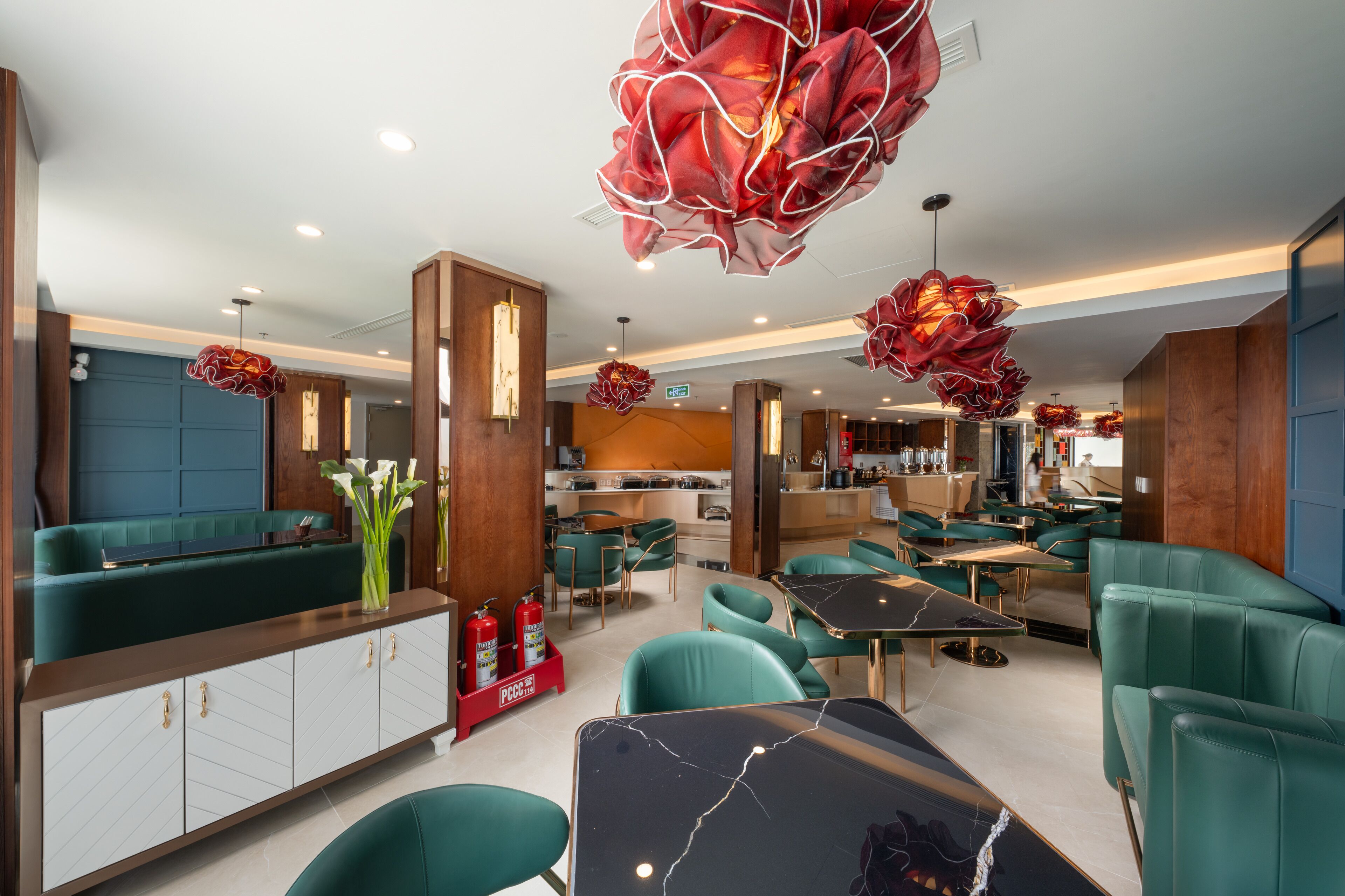 A modern restaurant interior with teal seating, marble tables, and unique red pendant lighting.