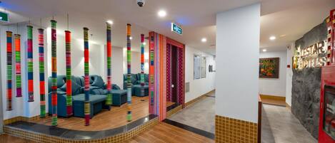 A hotel lobby with a seating area, a reception desk, and a staircase leading to the upper floor.