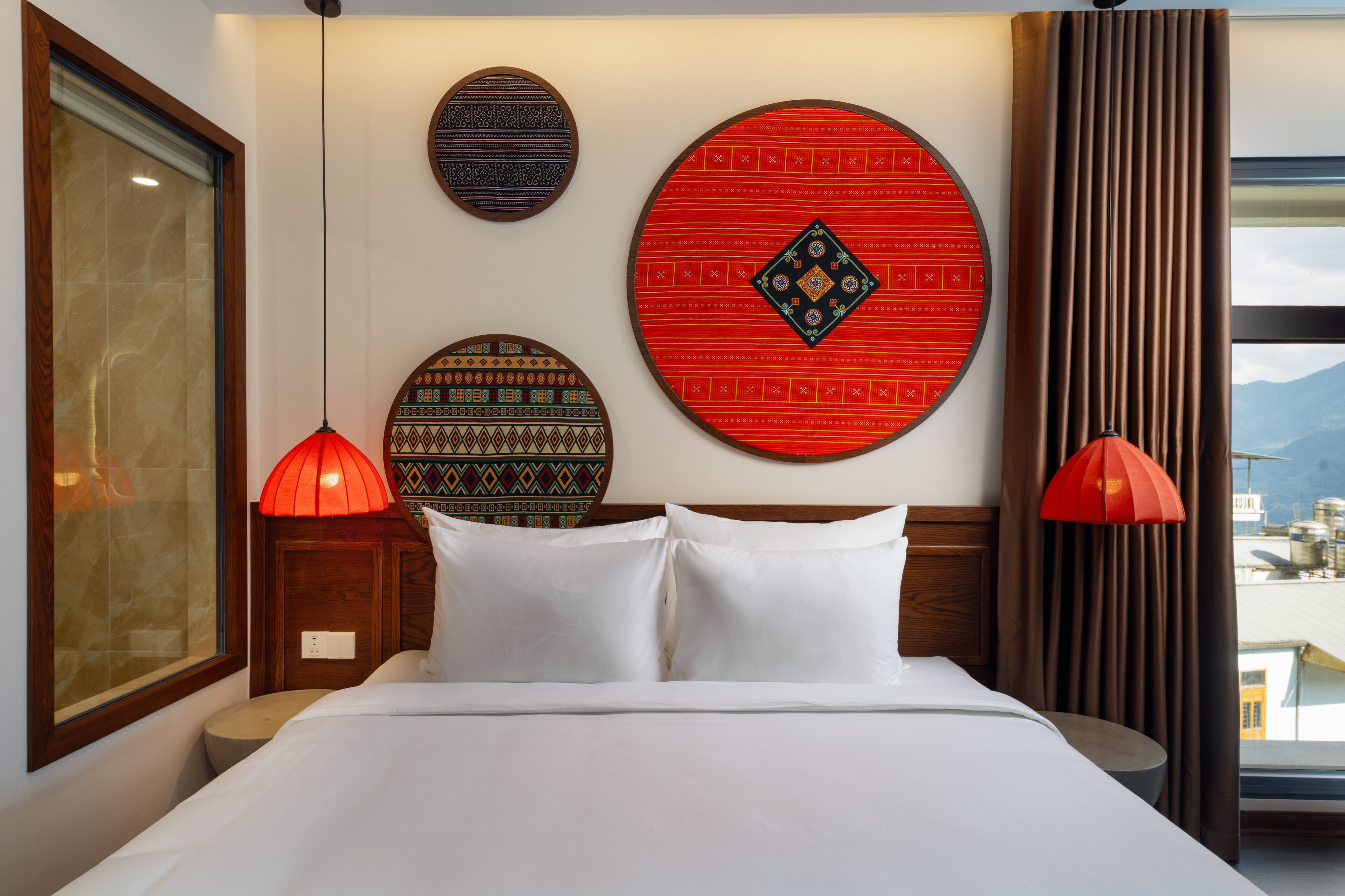A hotel room with a bed, two red pendant lights, and three decorative wall plates.