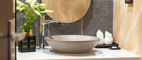 Un baño moderno con un espejo ovalado grande, un lavabo tipo cuenco y una pequeña planta en maceta.