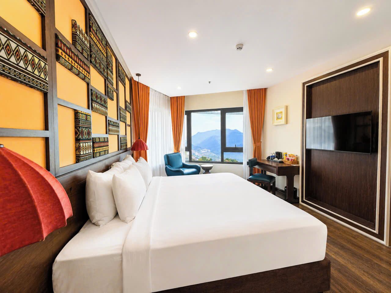 Habitación de hotel con una cama grande, un escritorio, una silla, un televisor y vistas a las montañas.