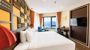 Ein Hotelzimmer mit einem großen Bett, einem Schreibtisch, einem Sessel, einem Fernseher und Blick auf die Berge.