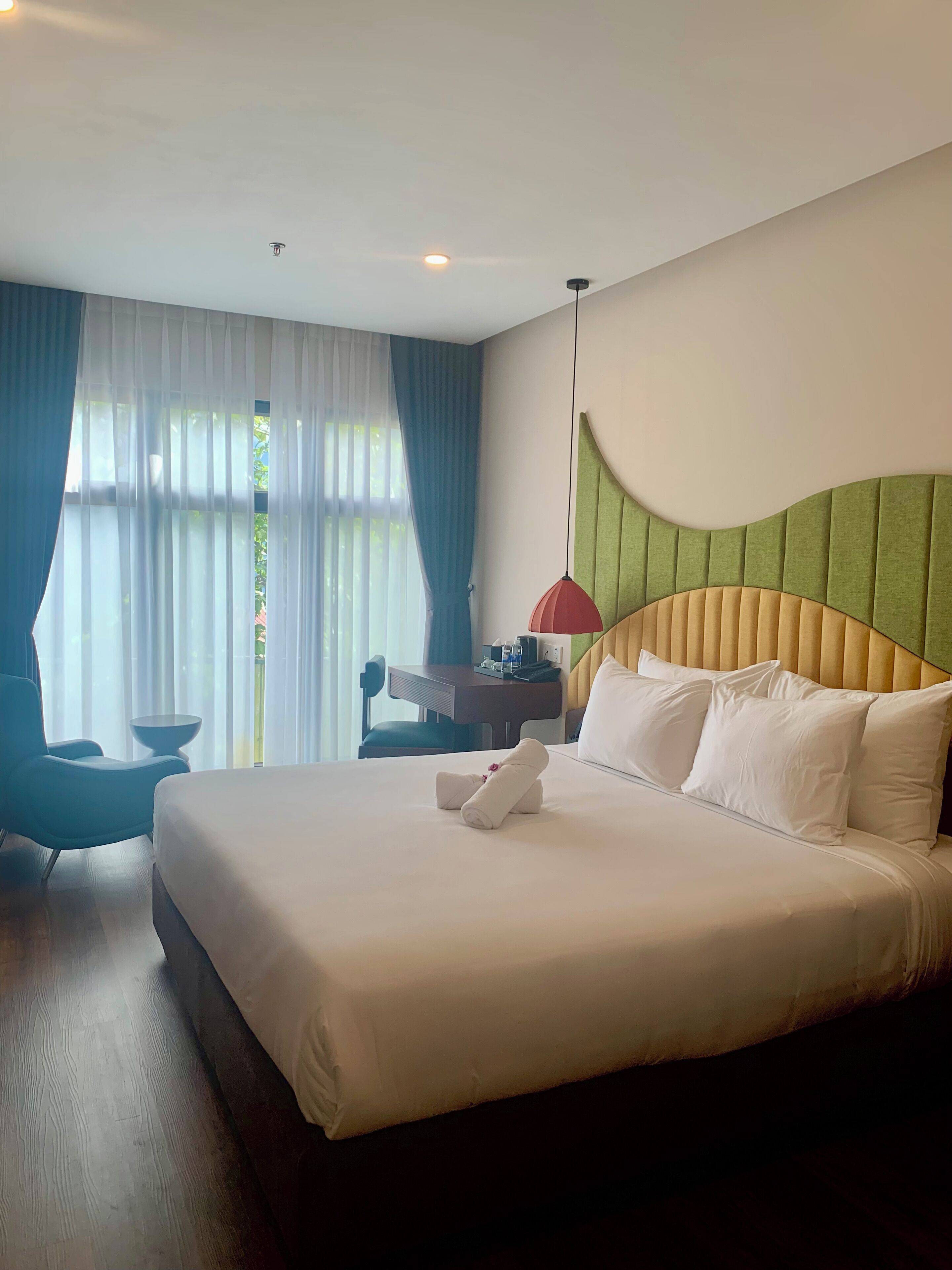 A hotel room with a large bed, a desk, a chair, and a window with curtains.