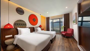 A hotel room with two beds, a red chair, a large window with a mountain view, and decorative wall art.