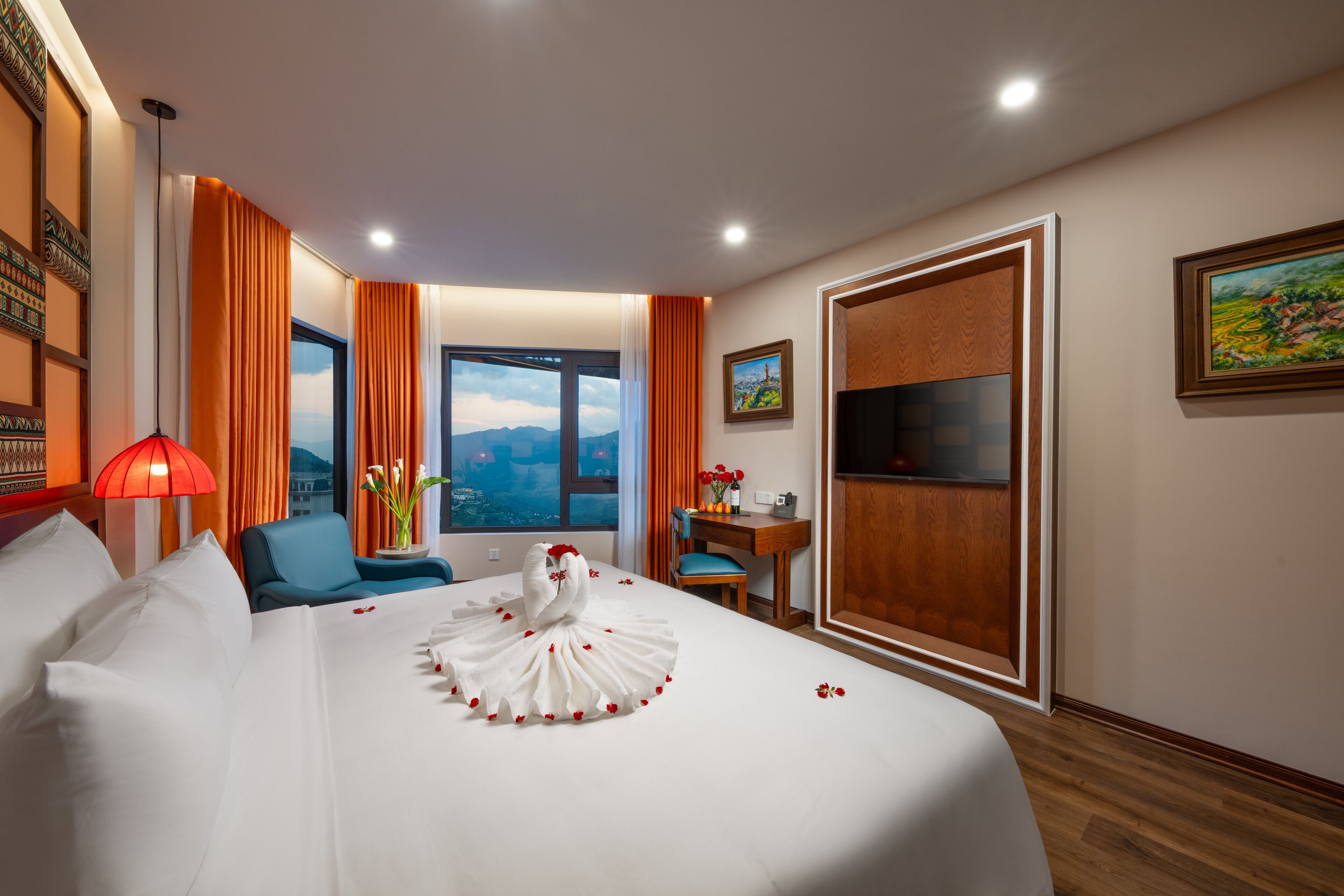 Ein Hotelzimmer mit einem großen Bett, einem Schreibtisch, einem Sessel, einem Fernseher und Blick auf Berge durch das Fenster.