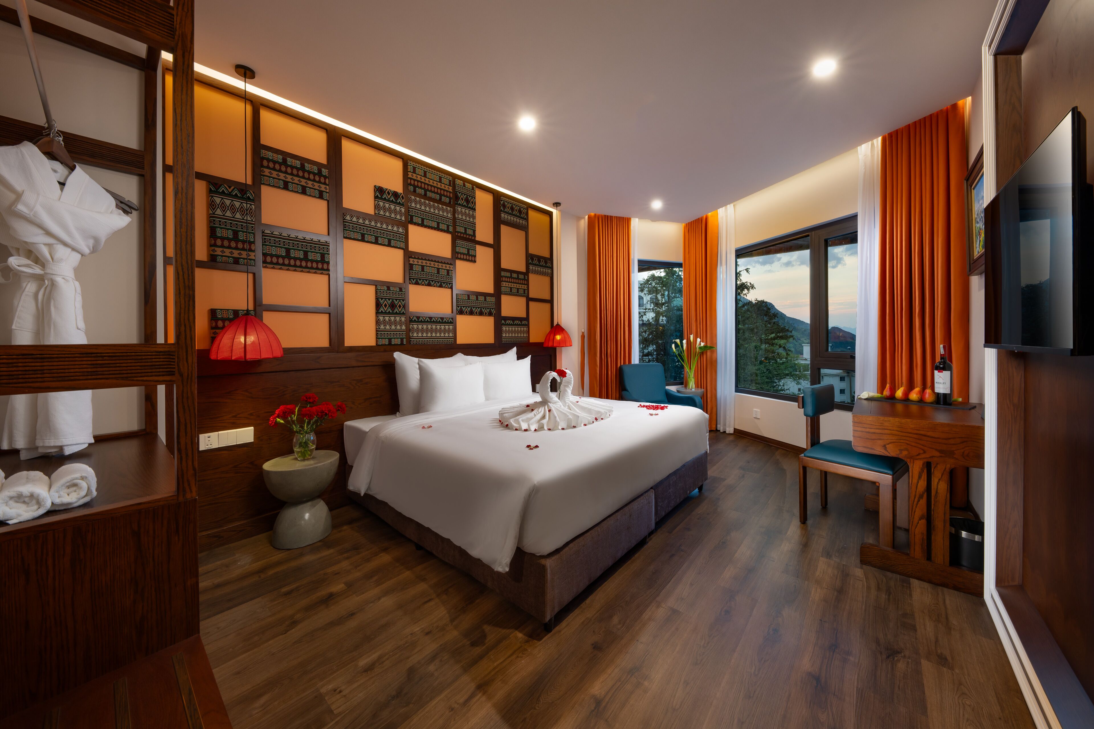 Habitación de hotel con una cama grande, cabecera de madera, mesita de noche con lámpara, televisión y vistas al exterior.