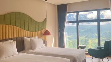 A hotel room with two beds, a large window with a mountain view, and a modern chair.