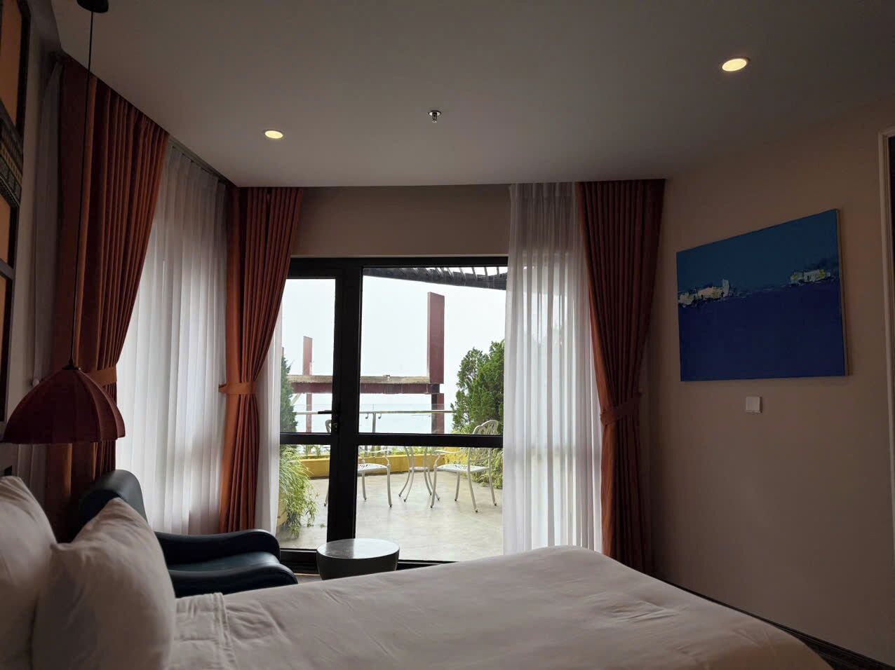 A hotel room with a large bed, a balcony with a view, and a painting on the wall.