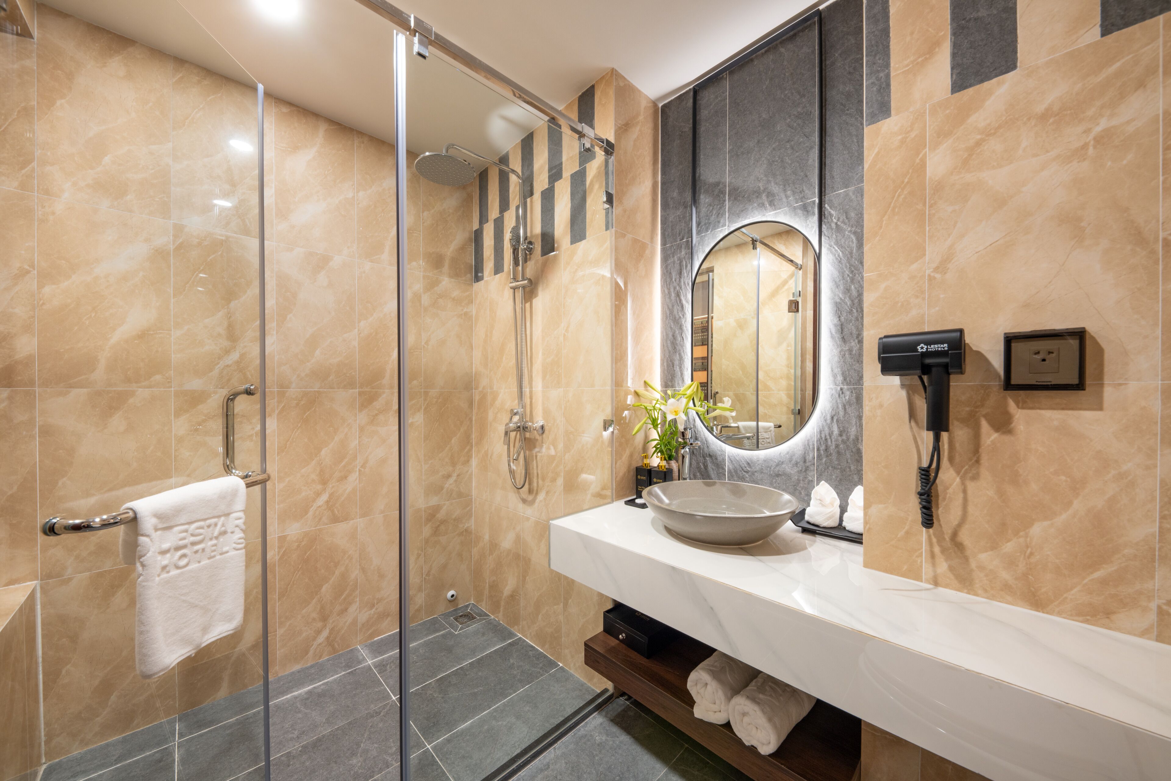 A modern bathroom with a glass shower enclosure, a white sink with a large mirror, and a towel rack.