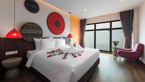 Habitación de hotel moderna con una cama grande, un elemento decorativo rojo en la pared, una lámpara colgante roja, suelo de madera y vistas a la montaña por la ventana.
