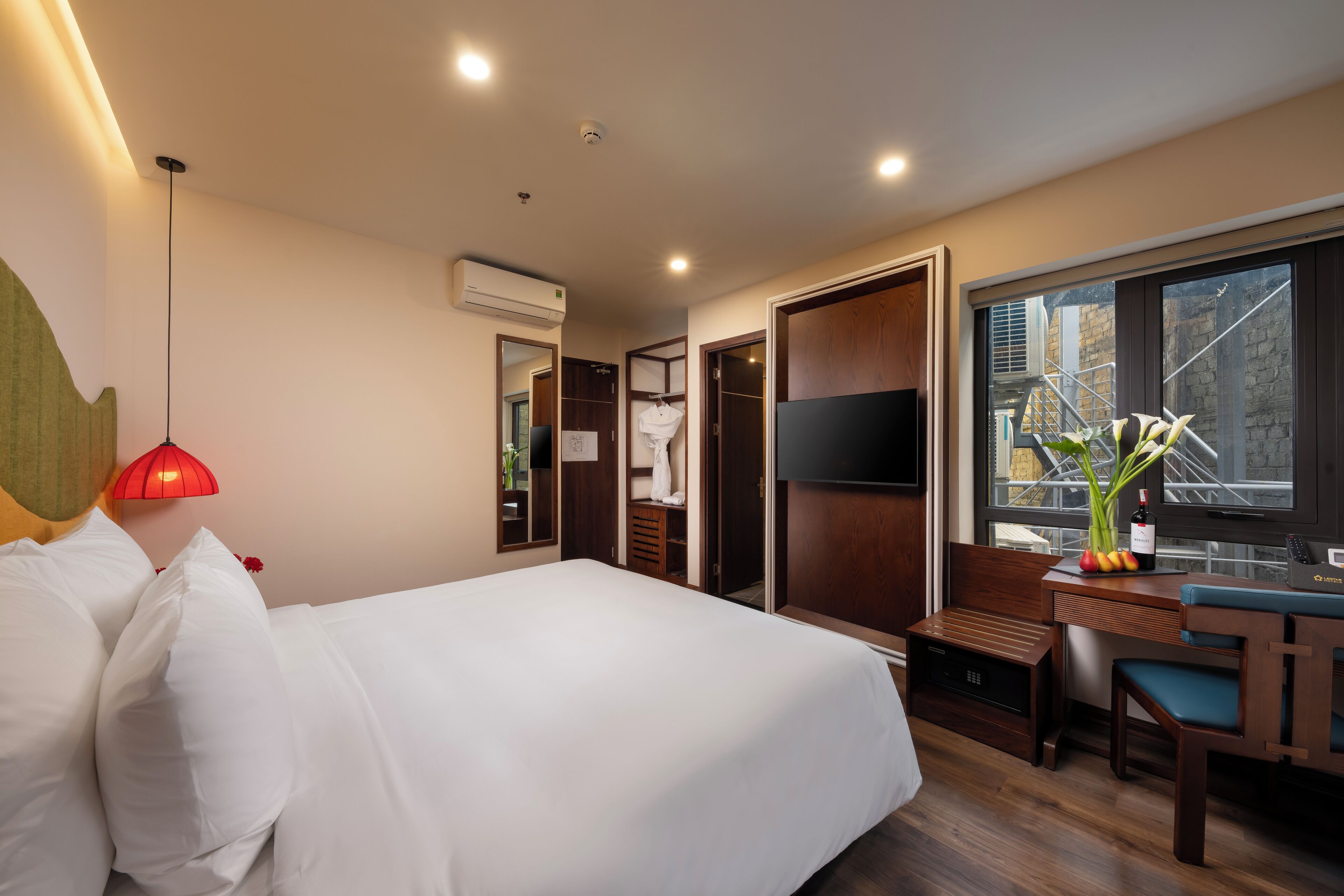 A hotel room with a bed, a desk, a chair, a TV, and a window with a view of the outside.