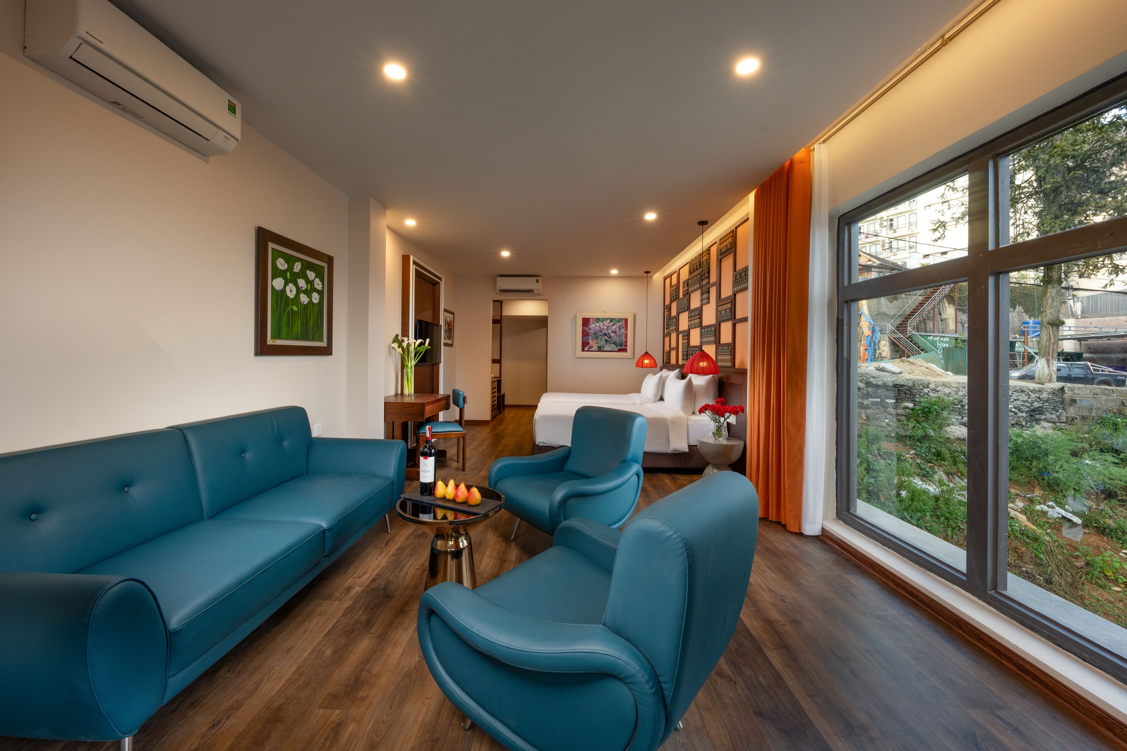 A modern living room with a blue sofa, two armchairs, a coffee table, and a view of a garden through large windows.