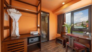 Une chambre d’hôtel avec une coiffeuse en bois, un peignoir, un bureau avec une chaise et une grande fenêtre donnant sur des immeubles.
