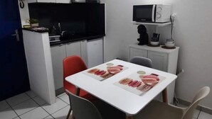 A compact kitchen with white cabinets, a microwave, and a television. There is a dining table with four chairs, and a blue door is visible to the left. - SCALE BOURBON SEASONAL RENTAL (Saint-Denis)