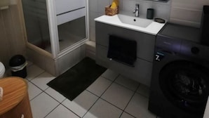 Une petite salle de bain avec un lavabo blanc, un miroir, des toilettes et un lave-linge.