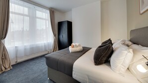 Una habitación de hotel con una cama grande, un armario y un ventanal con cortinas translúcidas.