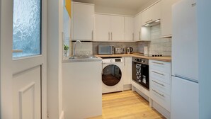 Una cocina compacta con armarios blancos, lavadora, microondas y estufa.