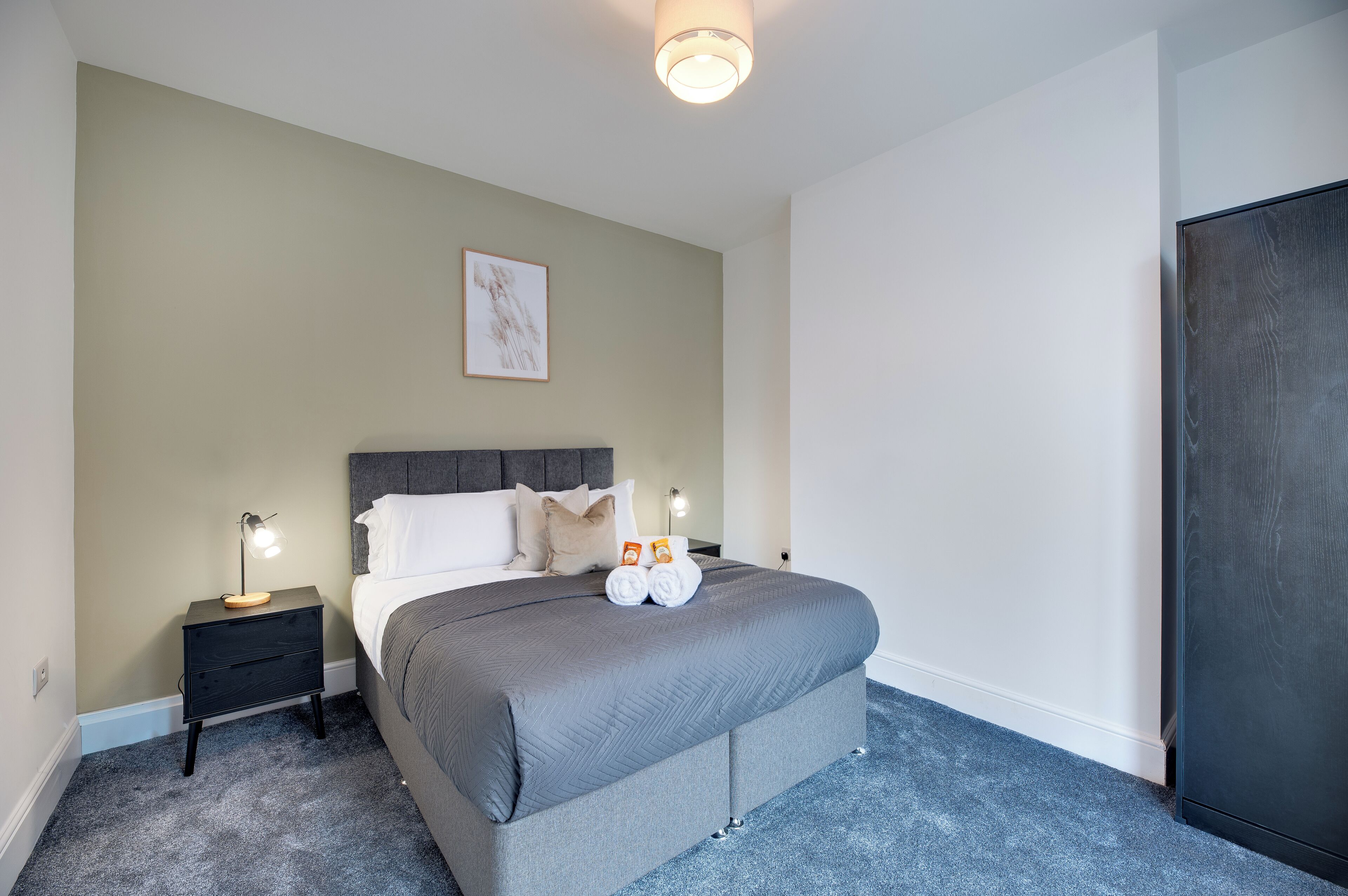 Une chambre à coucher avec un lit, une table de chevet, une lampe et un tableau encadré au mur.