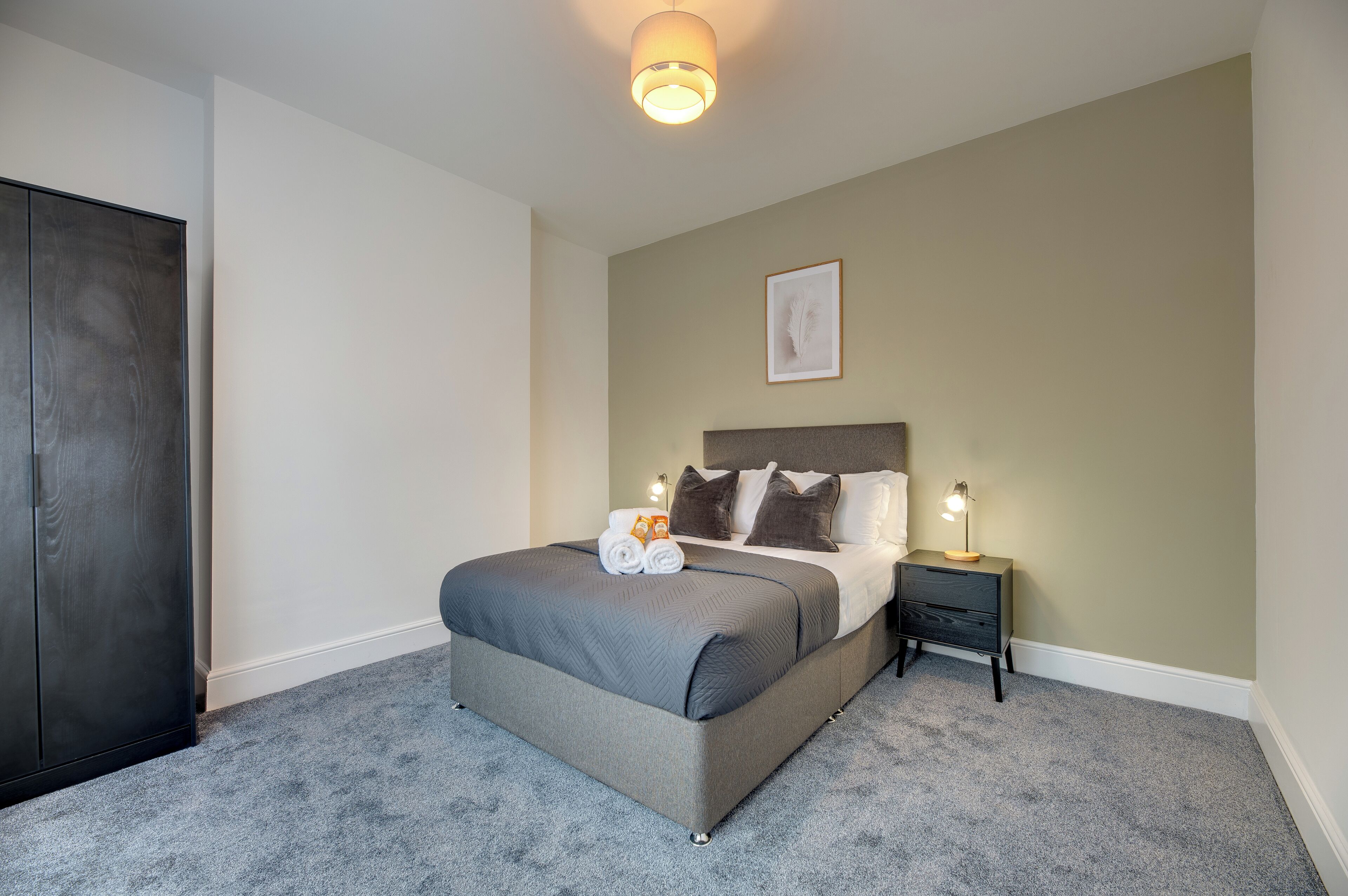 A neatly made bed with a grey headboard, a bedside lamp, and a framed picture on the wall.