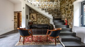 Una sala de estar con una escalera de piedra, un sofá, dos sillones y una alfombra estampada.