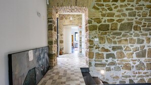 Un pasillo con paredes de piedra y suelo de baldosas, que conduce a una habitación con cama y ventana.