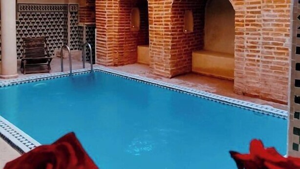 A swimming pool with a brick structure and arches, surrounded by a building with patterned walls and a skylight. - Riad sarsavti (Marrakech)