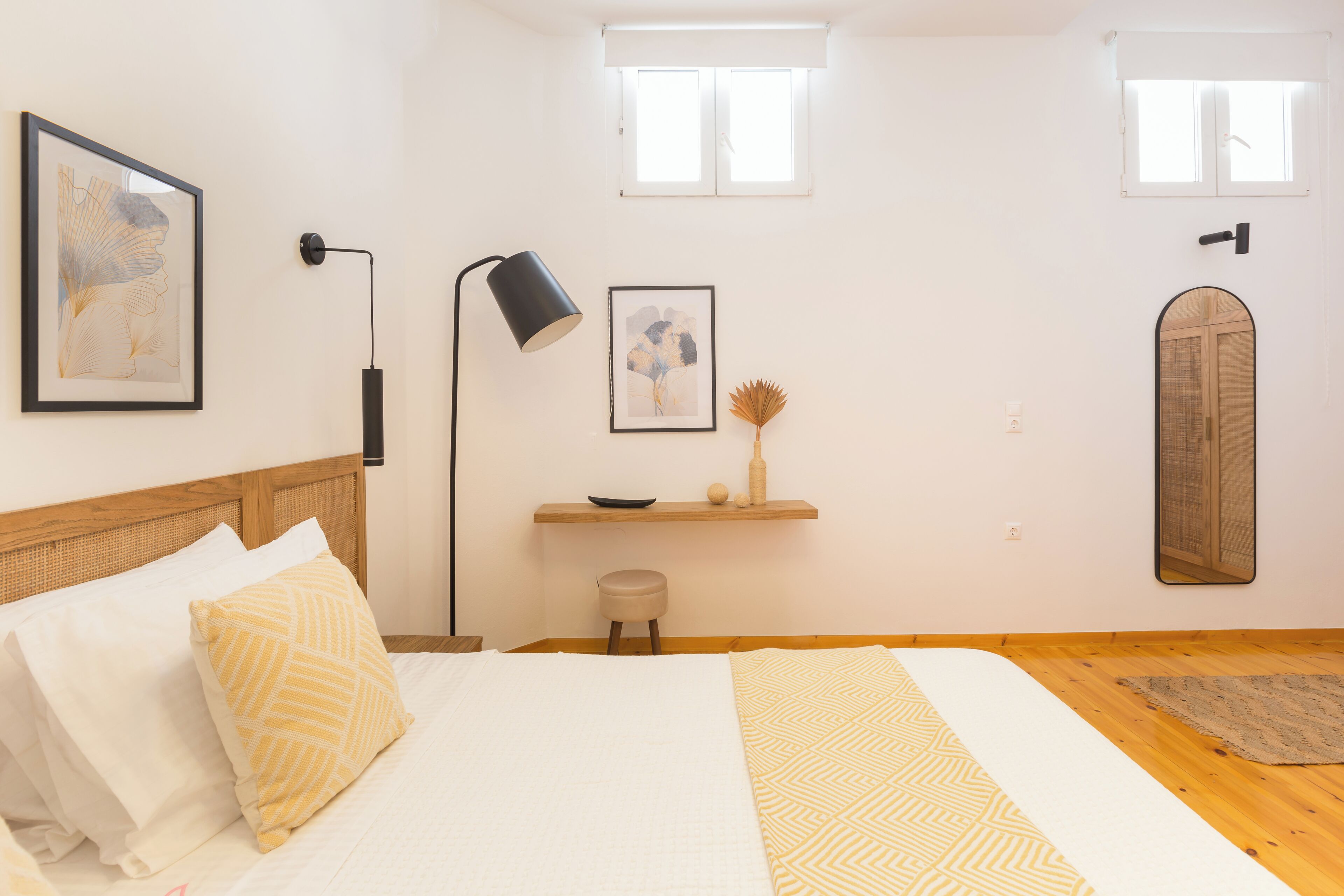 Ein Schlafzimmer mit Bett, Nachttisch, Lampe, Fenster und Spiegel.