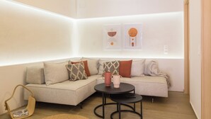 A modern living room with a sectional sofa, a round coffee table, and a small side table. There are abstract wall art pieces and a hanging light fixture. - Old Town Charm-Cozy 2BR with Rooftop (Rethymno)