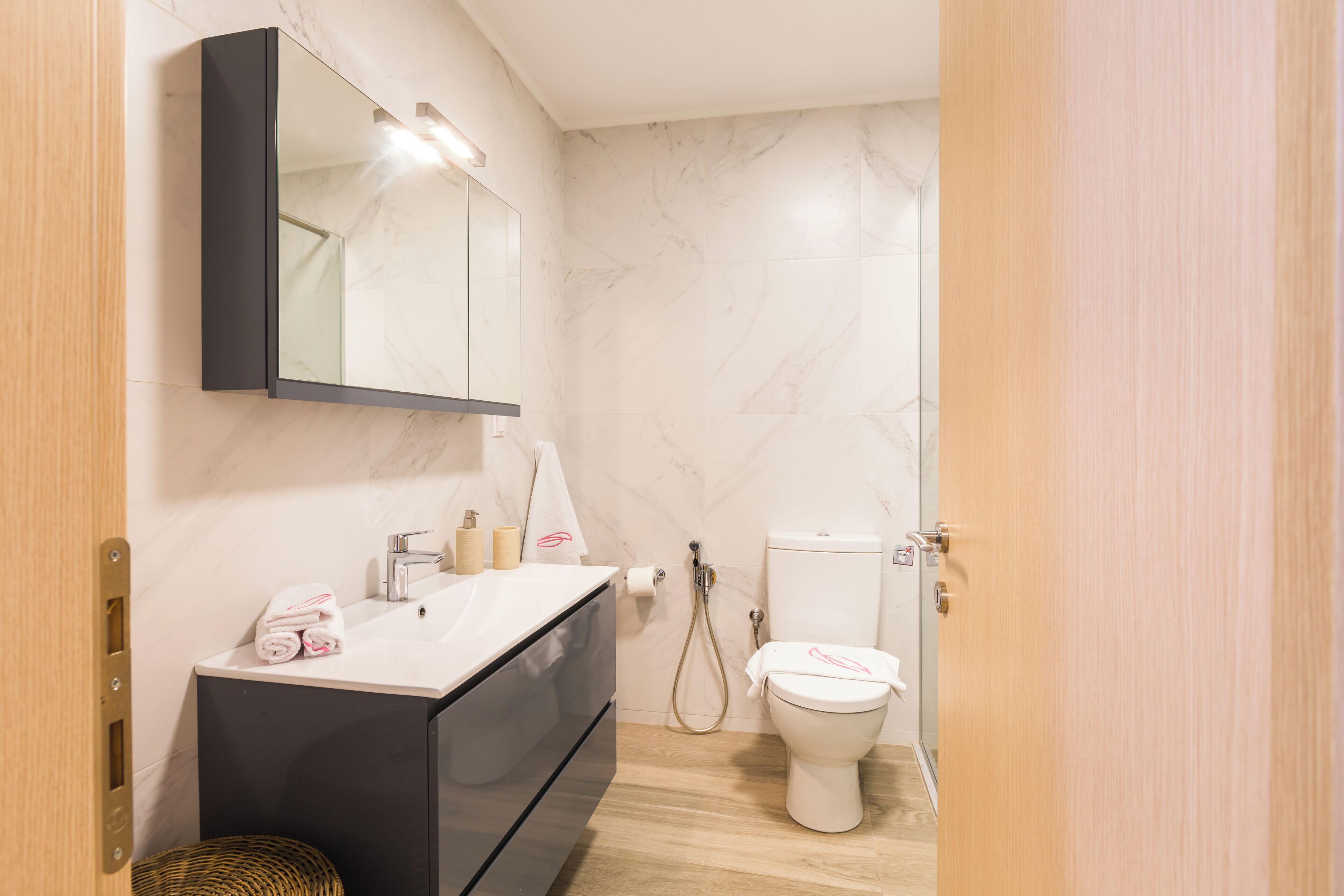 Ein modernes Badezimmer mit einer Marmorwand, einem schwarzen Waschtisch, einer Toilette und einer Dusche.