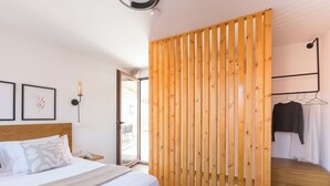 A bedroom with a bed, a wooden partition, a bedside table, a hanging clothes rack, and a view of the outside. - Old Town Charm-Cozy 2BR with Rooftop (Rethymno)