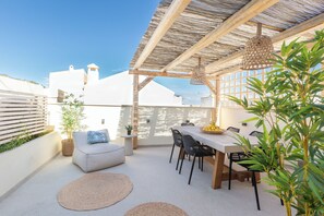 Een terras op het dak met een tafel en stoelen, een hanglamp en planten in potten.