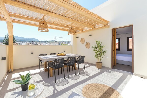 Een dak terras met een houten pergola, een eettafel met stoelen, een potplant en een uitzicht op de stad.