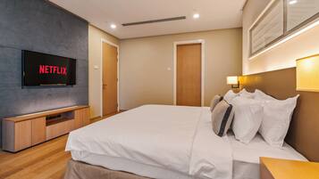 A modern hotel room with a large bed, a flat-screen TV mounted on the wall, a wooden bedside table, and a wall-mounted lamp.