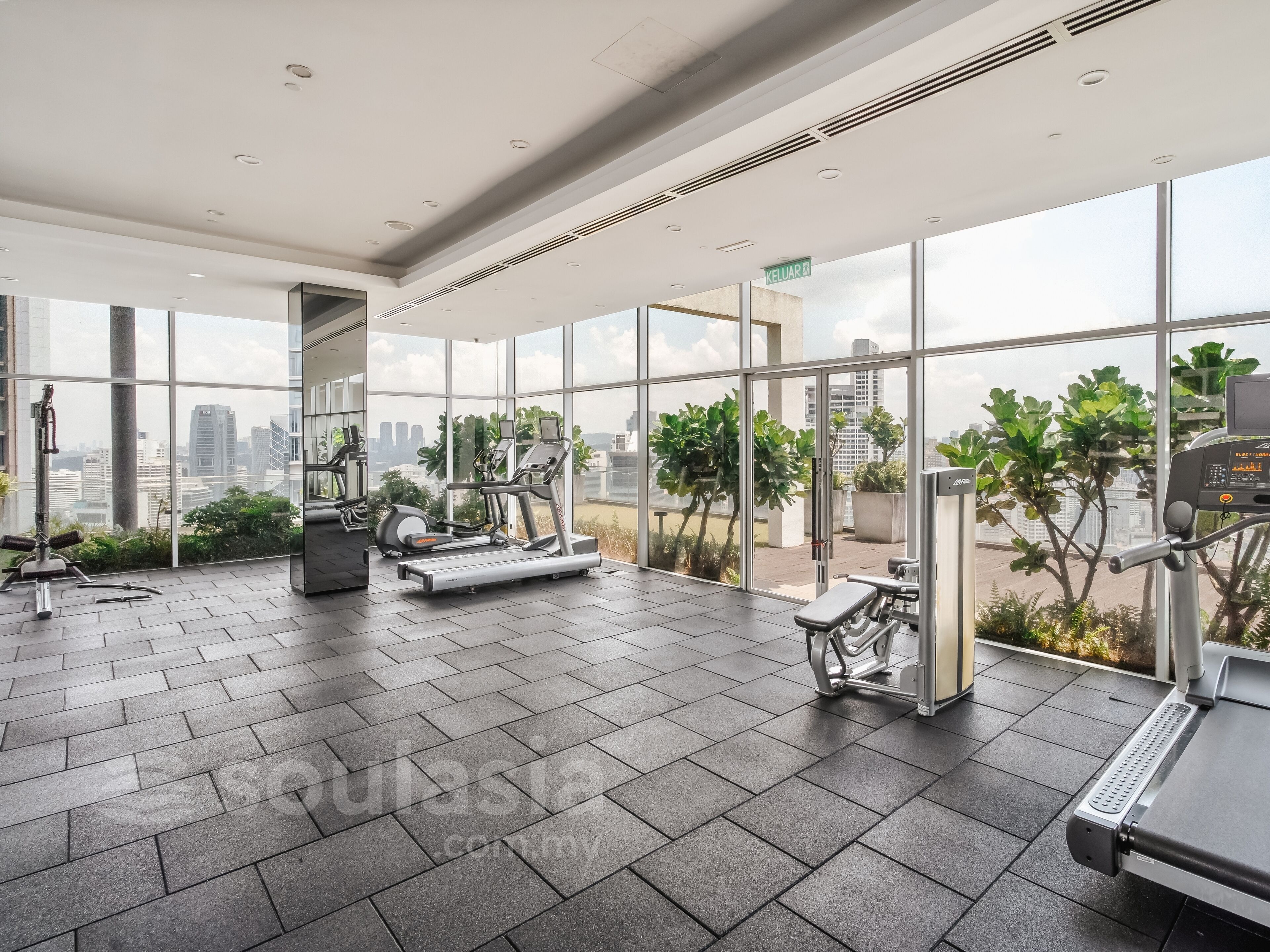 Un gimnasio moderno con equipo de ejercicio, ventanas amplias y vistas a la ciudad.