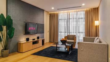 A modern living room with a flat-screen TV, a sofa, a coffee table, and a large window with curtains.