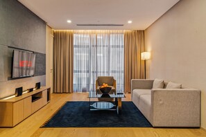 A modern living room with a flat-screen TV, a sofa, a chair, a coffee table, and a large window with curtains. - 188 Suites KLCC by Soulasia (Kuala Lumpur)