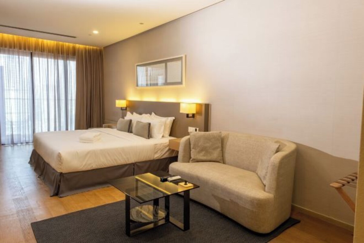 Una habitación de hotel con cama, sofá, una mesita y ventana con cortinas.