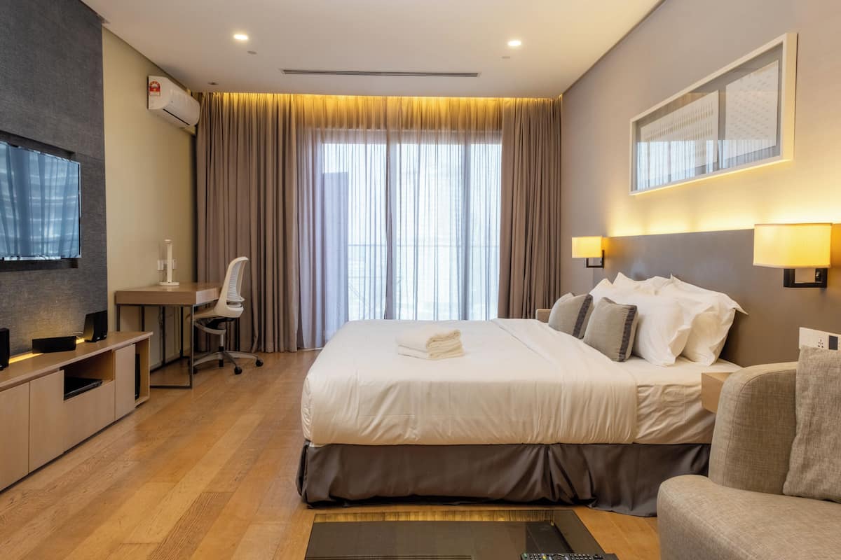 Habitación de hotel con una cama grande, un escritorio, una silla, un televisor y una ventana con cortinas.