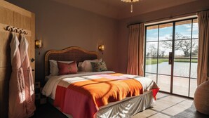 Un dormitorio con una cama grande, un armario de madera, un perchero y vistas a un cuerpo de agua a través de un ventanal amplio.