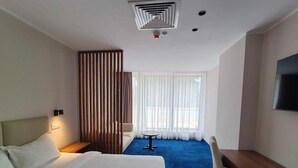 Una habitación de hotel con cama, escritorio, silla, televisión y ventana con cortinas.