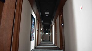 Un largo y estrecho pasillo de hotel con puertas de madera a ambos lados, un techo con iluminación empotrada y un letrero que indica la habitación número 202.