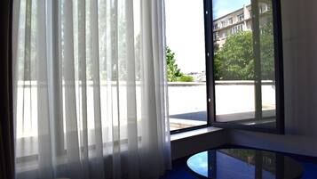 A room with a large window, sheer curtains, and a round glass table.