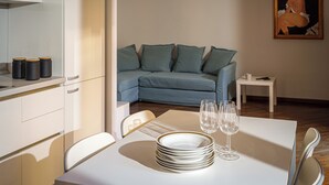 Uma área de jantar com mesa posta para quatro pessoas, um sofá ao fundo e um quadro na parede.