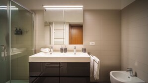 Casa de banho moderna com lavatório duplo, cabine de chuveiro em vidro e sanita higiênica separada.