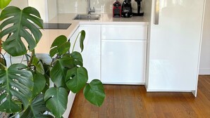 A modern kitchen with white cabinetry, a built-in oven, a sink, and a coffee maker. - L'appartement Colombier (Paris)