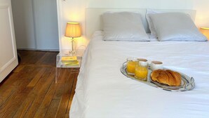 A neatly made bed with white linens, a tray with croissants and orange juice, and a bedside lamp on a clear nightstand. - L'appartement Colombier (Paris)