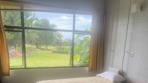 Une chambre avec deux lits, une petite table, une chaise et une fenêtre donnant sur un jardin.