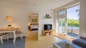Ein modernes Wohnzimmer mit Essbereich, Fernseher und einer großen Glasschiebetür zum Außenbereich.