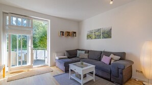 Ein modernes Wohnzimmer mit einem grauen Sofa, einem weißen Beistelltisch und einer Glastür, die auf einen Balkon führt.