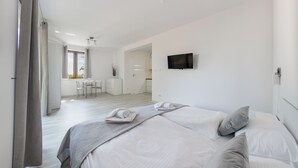 A modern bedroom with a large bed, a TV mounted on the wall, and a view of the dining area through an open door. - Apartamenty Sun & Snow Zasypane Mazury (gmina Malkinia Gorna)